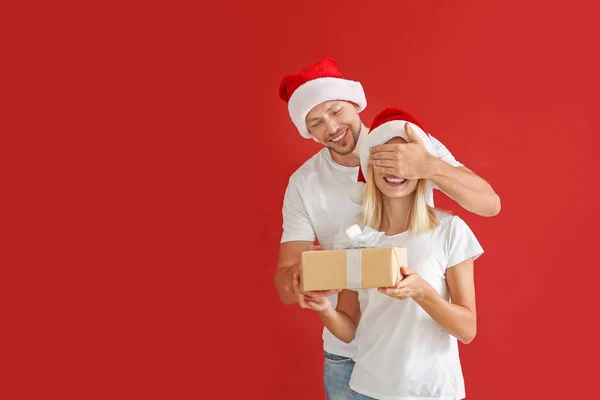 Husband giving Christmas present to his wife against color background — Stock Photo, Image