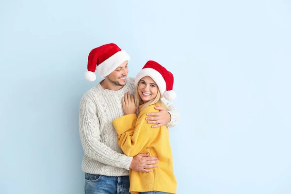 Casal feliz em chapéus de Papai Noel em fundo de cor — Fotografia de Stock