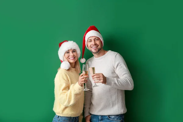 Feliz pareja en los sombreros de Santa beber champán sobre fondo de color — Foto de Stock
