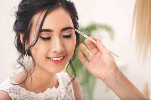 Truccatore professionista che lavora con la giovane sposa asiatica a casa — Foto Stock