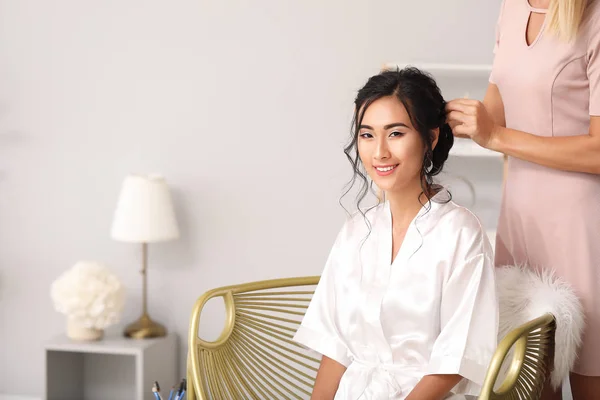 Cabeleireiro profissional trabalhando com a jovem noiva asiática em casa — Fotografia de Stock