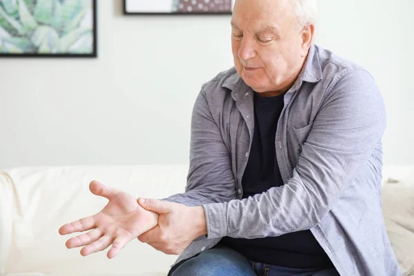 Senior man suffering from pain in wrist at home — Stock Photo, Image