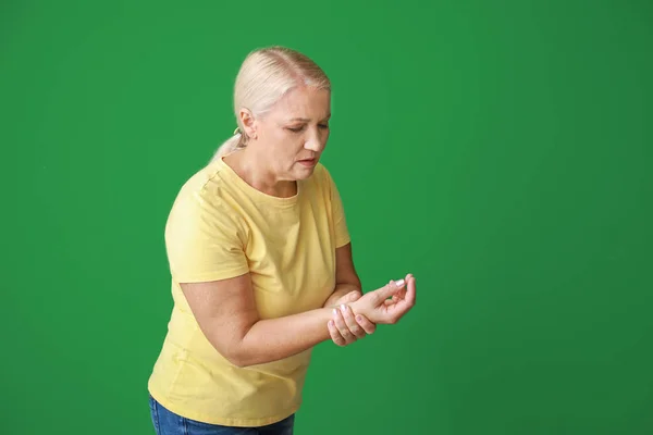 Reife Frau leidet unter Schmerzen im Handgelenk auf farbigem Hintergrund — Stockfoto