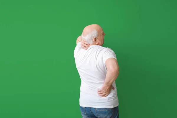 Старший мужчина страдает от болей в спине на цветном фоне — стоковое фото