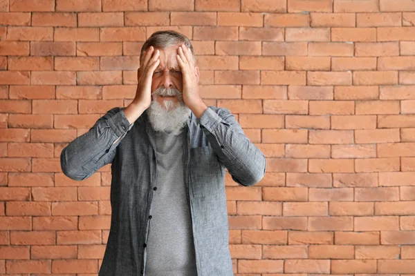 Senior man suffering from headache against brick wall — Stock Photo, Image