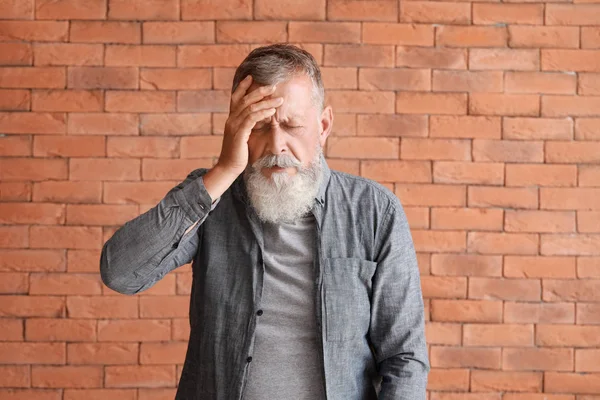 Homem idoso que sofre de dor de cabeça contra a parede de tijolo — Fotografia de Stock