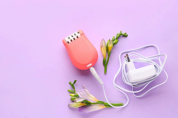 Modern epilator with charger and flowers on color background — Stock Photo, Image