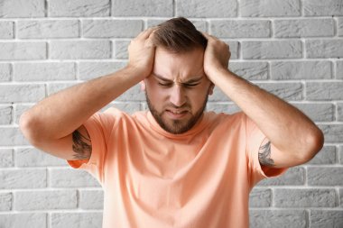 Genç adam gri tuğla duvardan dolayı baş ağrısı çekiyor.