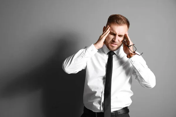 Young businessman suffering from headache on grey background — Stock Photo, Image