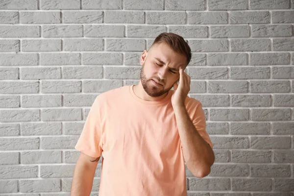 Mladý muž trpí bolestí hlavy proti šedé cihlové zdi — Stock fotografie