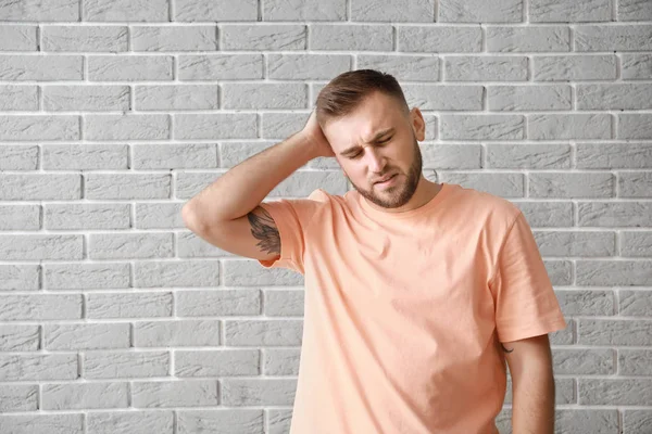 Young man suffering from headache against grey brick wall — Stock Photo, Image