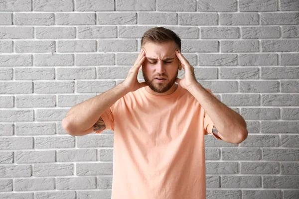 Jeune homme souffrant de maux de tête contre un mur de briques grises — Photo