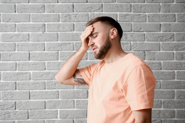 Fiatalember szenved fejfájás ellen szürke téglafal — Stock Fotó