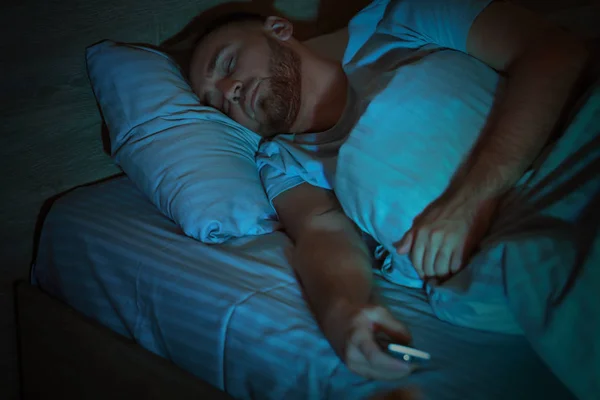 Young man with TV remote control sleeping in bed at night — Stock Photo, Image