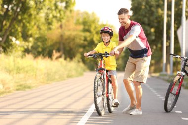 Baba oğluna dışarıda bisiklete binmeyi öğretiyor.