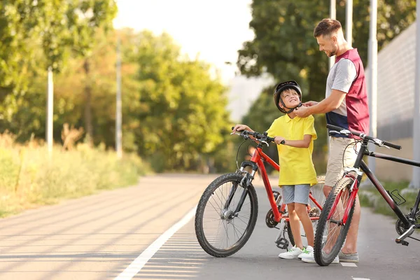 Батько допомагає синові одягнути велосипедний шолом на відкритому повітрі — стокове фото