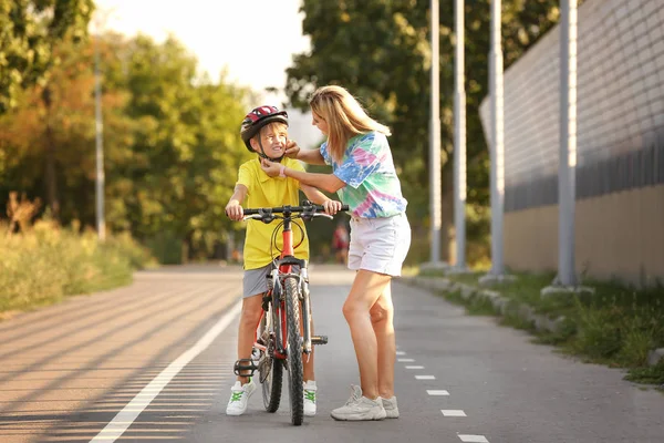 Mãe ajudando seu filho a colocar em capacete de bicicleta ao ar livre — Fotografia de Stock