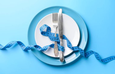 Plakalı çatal bıçak takımı ve renkli arka planda mezura. Diyet kavramı