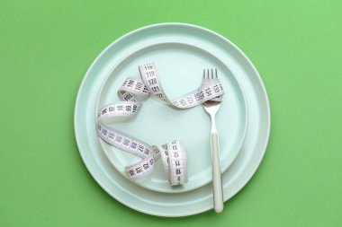 Plakalı çatal ve renkli arka planda mezura. Diyet kavramı