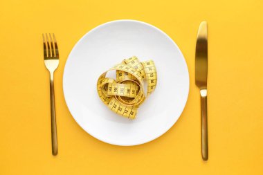 Plakalı çatal bıçak takımı ve renkli arka planda mezura. Diyet kavramı