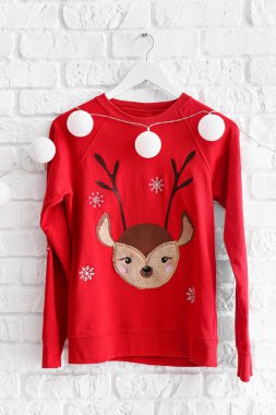 Beyaz tuğlalı duvarda Noel süveteri ve çelenk olan askı