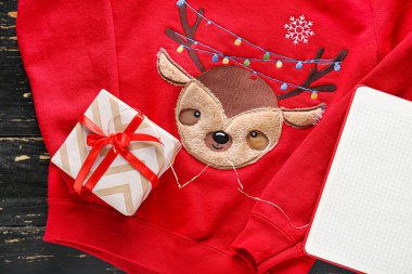 Tahta arka planda hediye paketi olan Noel kıyafetleri.
