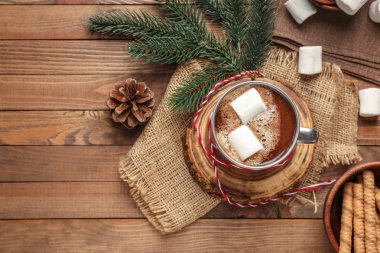 Bir fincan sıcak çikolata, marşmelov ve ahşap arka planda tatlılar.