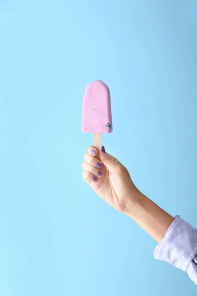 Female hand with tasty blueberry ice cream on color background — ストック写真