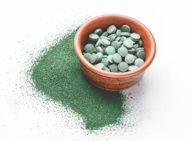 Sarmaşık hapları ve beyaz arka planda pudra dolu bir kase.