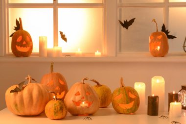 Pencerenin yanındaki masada Cadılar Bayramı balkabakları ve mumları