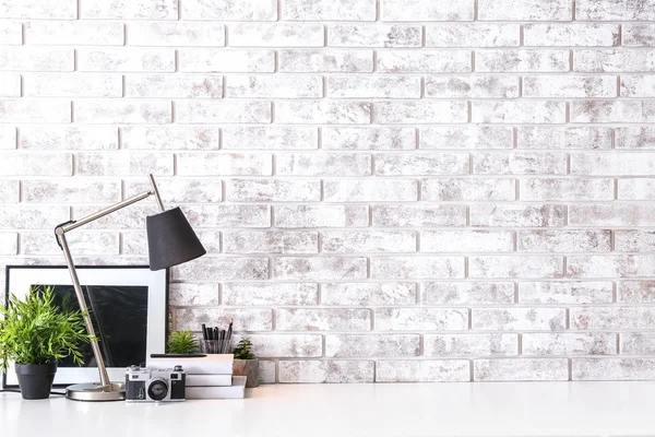 Lambalı, fotoğraf makineli, kitaplı ve tuğla duvarlı rahat bir iş yeri.