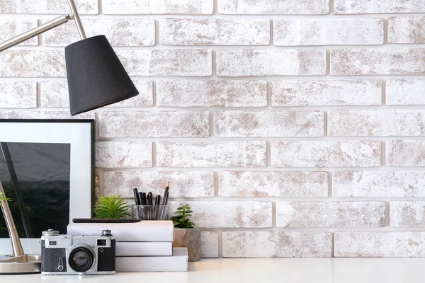Comfortable workplace with lamp, photo camera, books and decor near brick wall — Stock Photo, Image