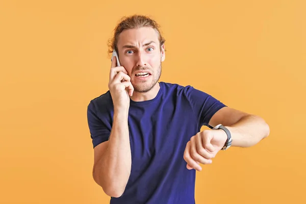 Stressed man talking by phone while looking at watch on color background — Stock Photo, Image