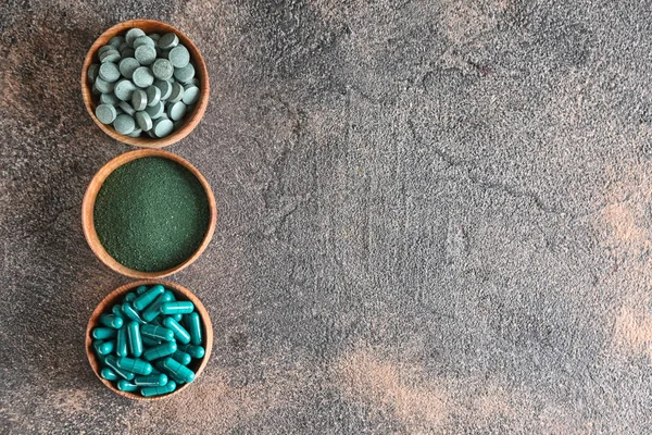 Bowls with spirulina powder and pills on grey background — Stock Photo, Image