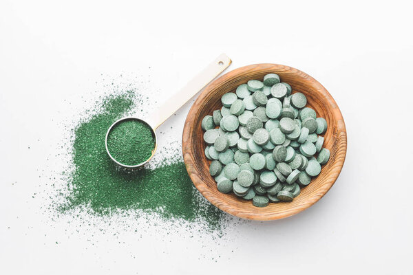 Чаша со спирулиной таблетки и порошок на белом фоне
