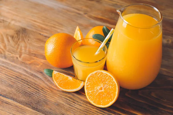 Glass and jug of fresh orange juice on wooden table — Stock Photo, Image