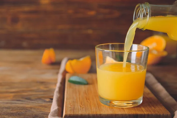 Χύτευση φρέσκου χυμού πορτοκαλιού σε ποτήρι στο τραπέζι — Φωτογραφία Αρχείου