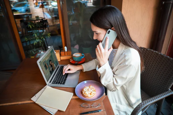 Female fashion blogger with laptop talking by phone in cafe — Stock Photo, Image