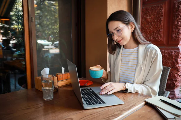 Young woman with laptop drinking coffee in cafe — Stock Photo, Image