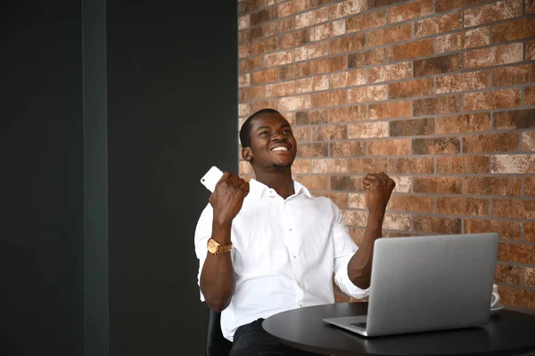 Homem afro-americano feliz com telefone celular e laptop no café — Fotografia de Stock