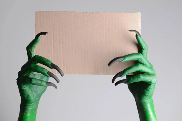 Hands of witch holding blank paper sheet on grey background. Halloween celebration — Stock Photo, Image