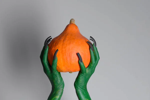 Mani di strega che tengono la zucca su sfondo grigio. Festa di Halloween — Foto Stock