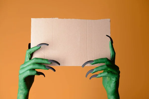Manos de bruja sosteniendo hoja de papel en blanco sobre fondo de color. Halloween celebración —  Fotos de Stock