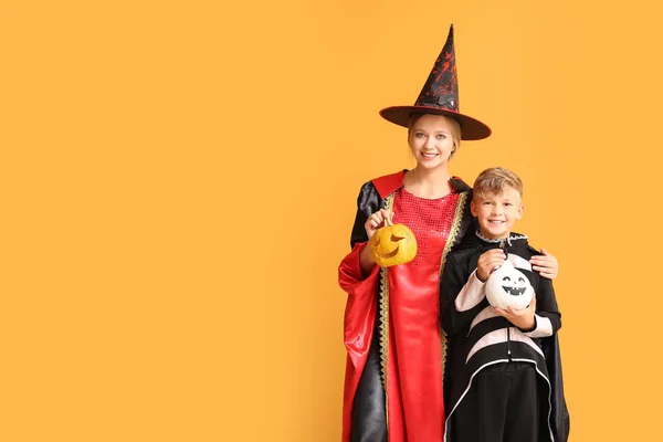 Mãe com filho pequeno em trajes de Halloween e com abóboras no fundo de cor — Fotografia de Stock