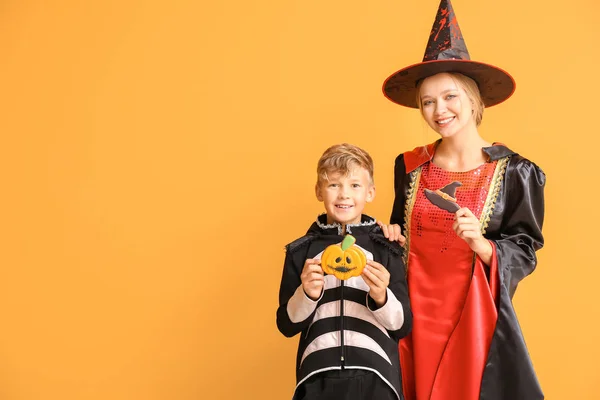 Madre con hijo pequeño en disfraces de Halloween y con galletas en el fondo de color —  Fotos de Stock