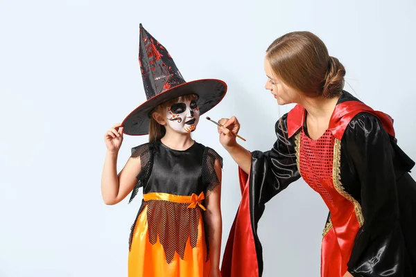 Mutter mit kleiner Tochter in Kostümen bereitet sich auf Halloween-Party auf hellem Hintergrund vor — Stockfoto