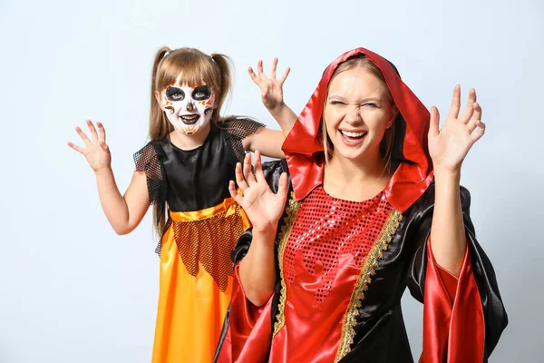 Mutter mit kleiner Tochter in Halloween-Kostümen auf hellem Hintergrund — Stockfoto