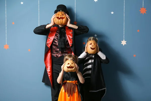 Father with children in Halloween costumes and with pumpkins on color background — Stock Photo, Image
