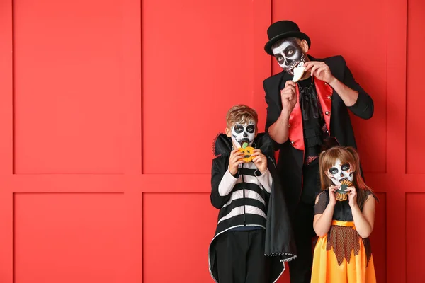 Father with children in Halloween costumes eating cookies on color background — Stock Photo, Image