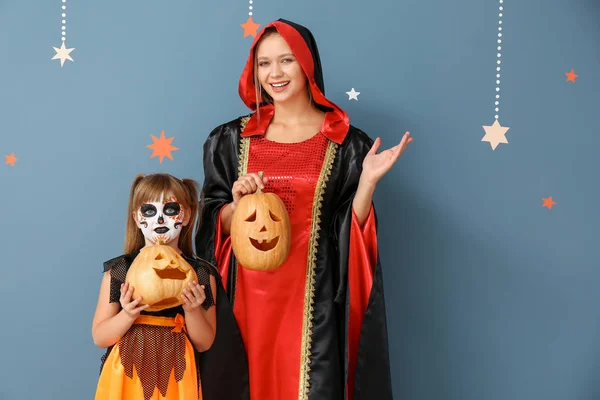 Mãe com pequena filha em trajes de Halloween e com abóboras no fundo de cor — Fotografia de Stock